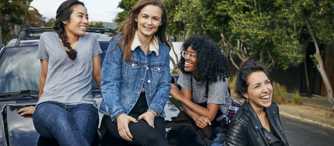 Picture of 4 young women laughing and smiling while sitting on the front of a car